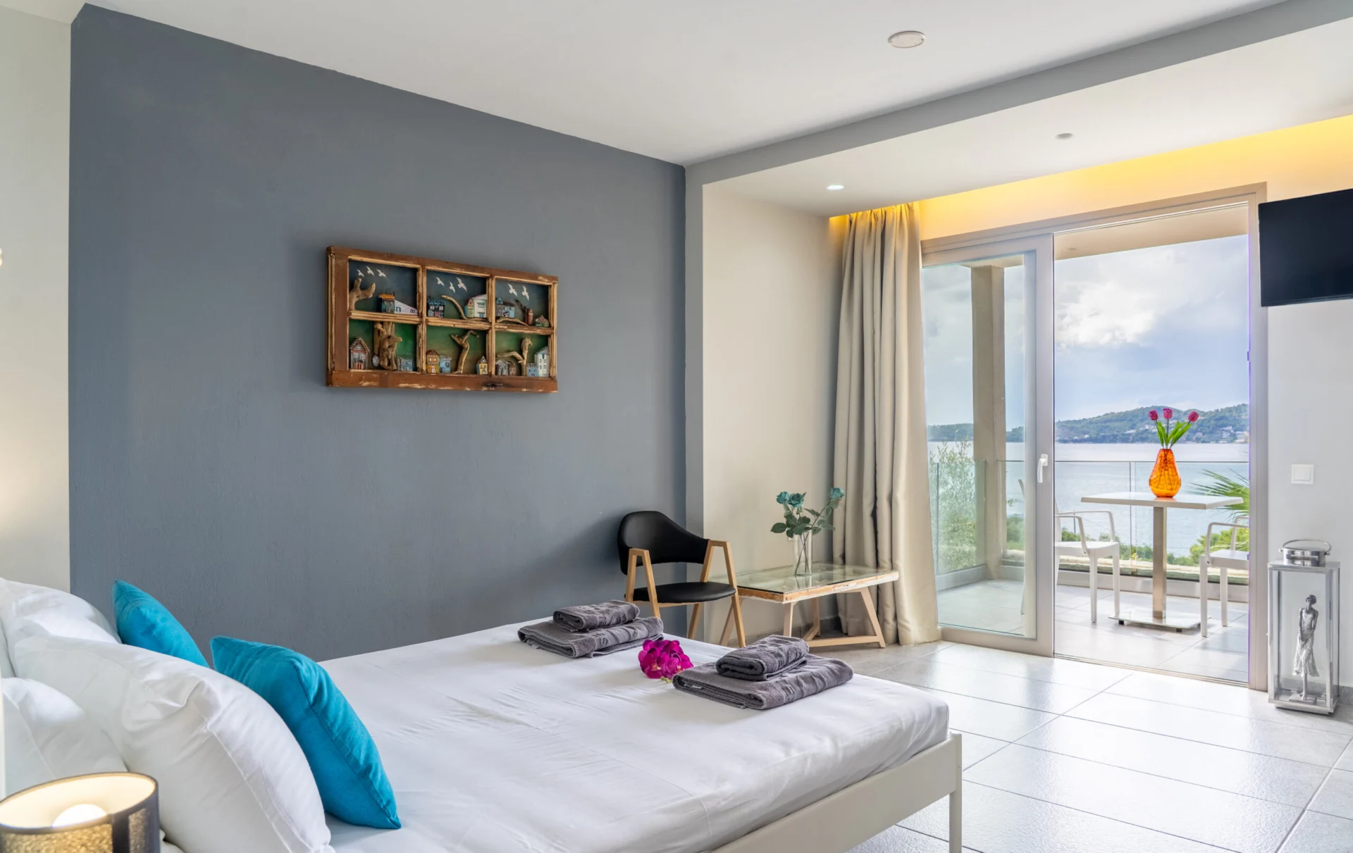 A bedroom with teal cushions and the terrace door open to the sea in the Alex 1 Classic Suite at CORE Luxury Suites, Skiathos.