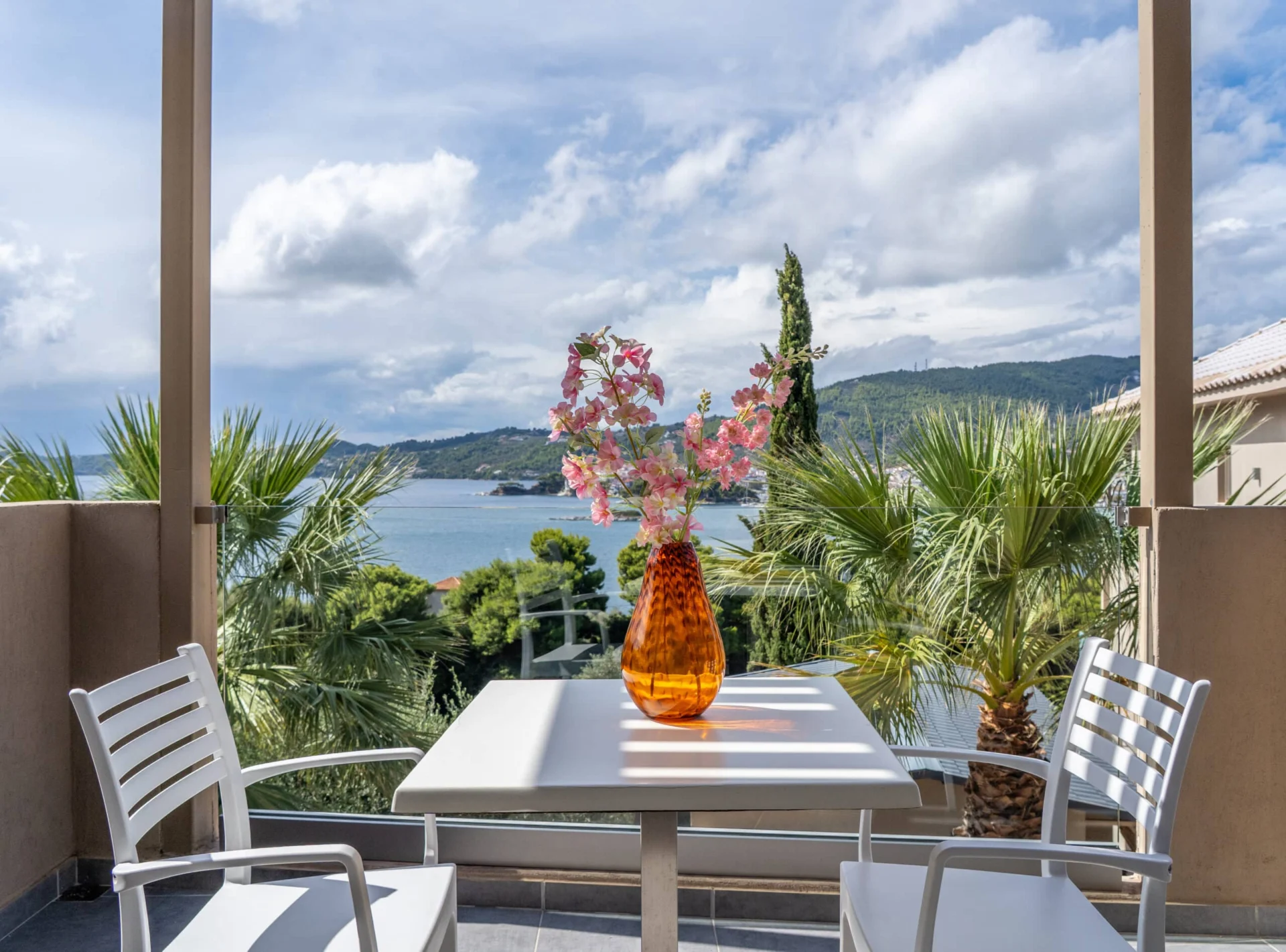 A balcony table with the sea framed by palms in the Alex 2 Deluxe Suite at CORE Luxury Suites, Skiathos.