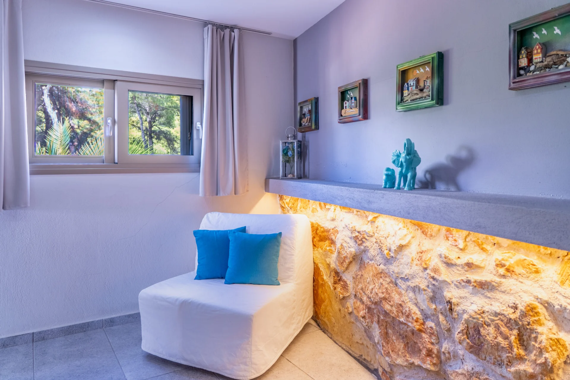 A seating area in lilac with a lit stone feature wall and blue cushions in the Alex 2 Deluxe Suite at CORE Luxury Suites, Skiathos.
