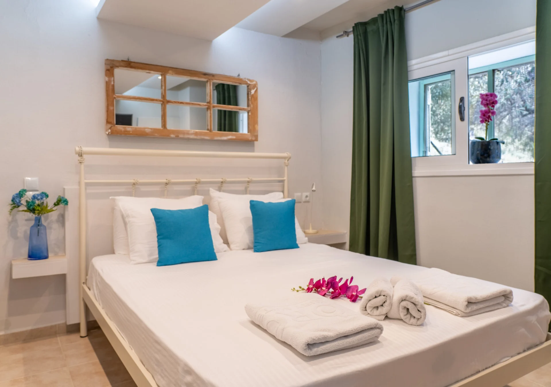 Un letto con testiera in legno, cuscini color ottanio e uno specchio nella Alex 3 Superior Suite di CORE Luxury Suites, Skiathos.