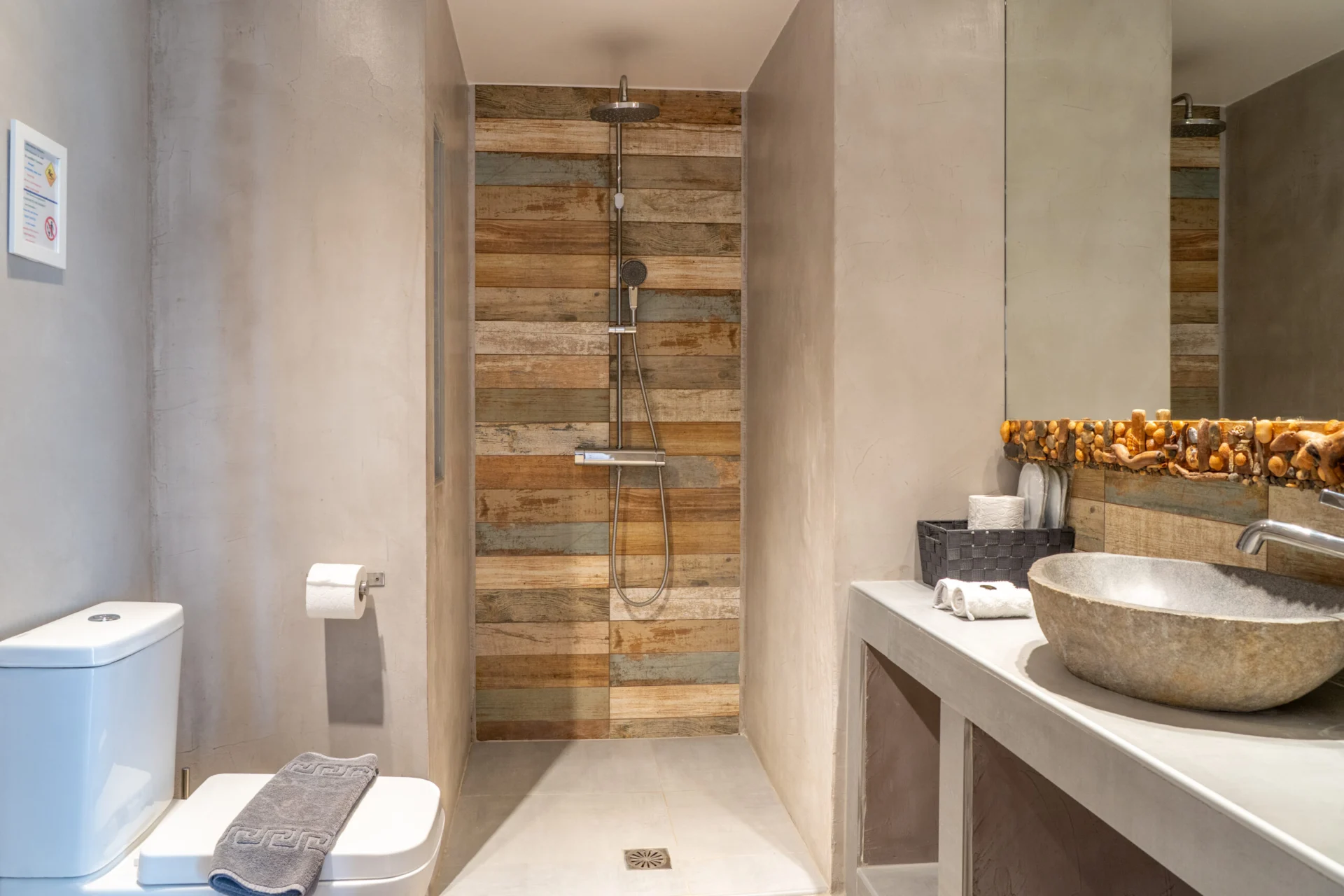 A bathroom with a reclaimed-wood rain shower and a carved stone basin in the Daniel Signature Suite at CORE Luxury Suites, Skiathos.