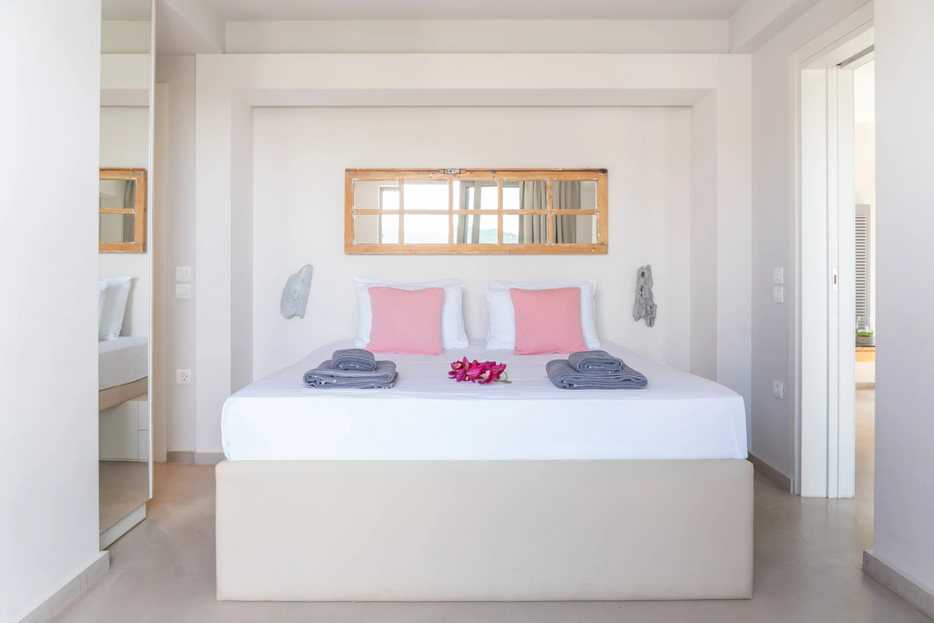 A bedroom in white linen with a mirror set beside the window in the Daniel Signature Suite at CORE Luxury Suites, Skiathos.