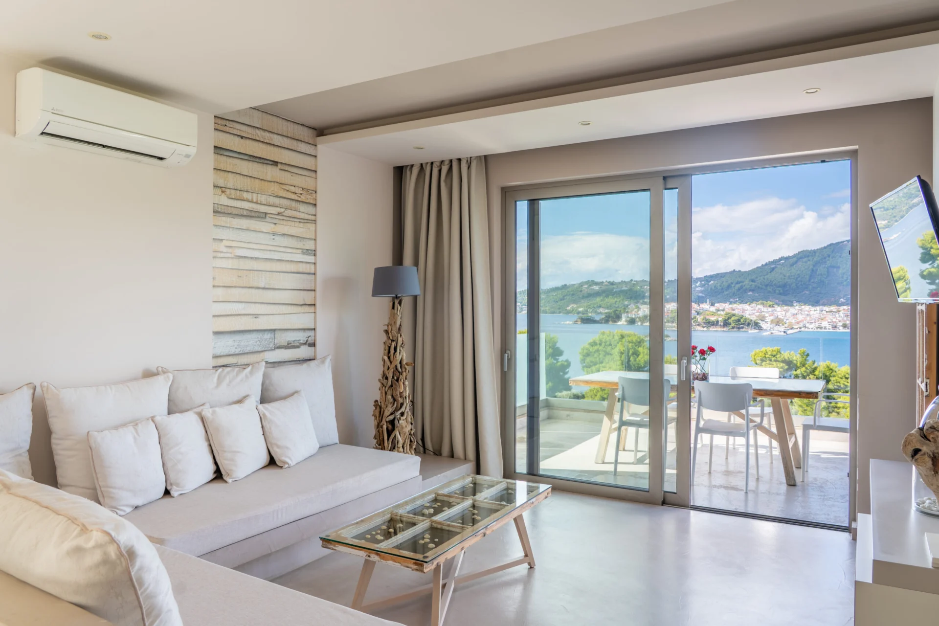 A living room with the terrace doors folded open to the pines and the sea in the Daniel Signature Suite at CORE Luxury Suites, Skiathos.