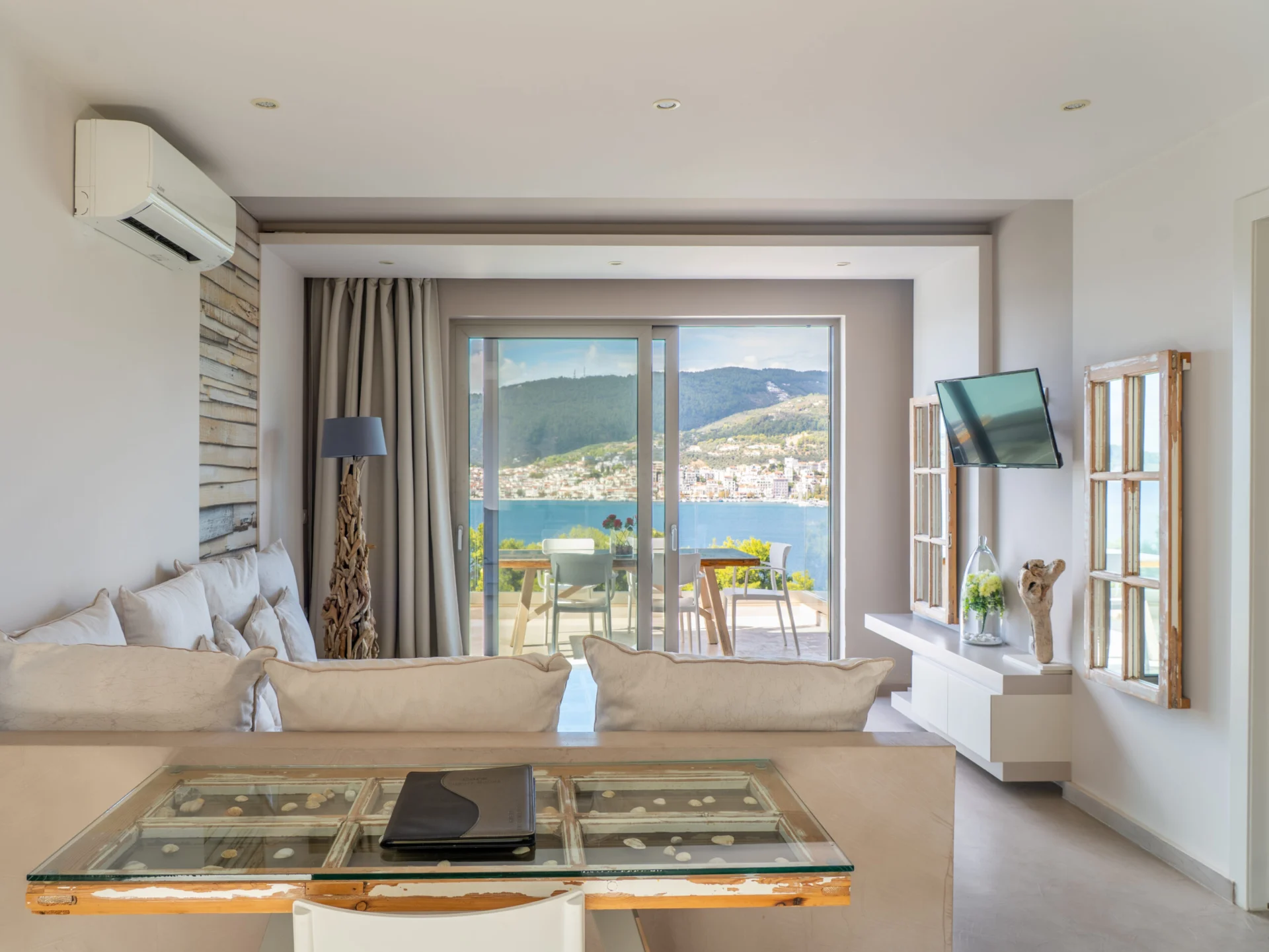A living room with a low sofa, a glass table and the bay through the terrace doors in the Daniel Signature Suite at CORE Luxury Suites, Skiathos.