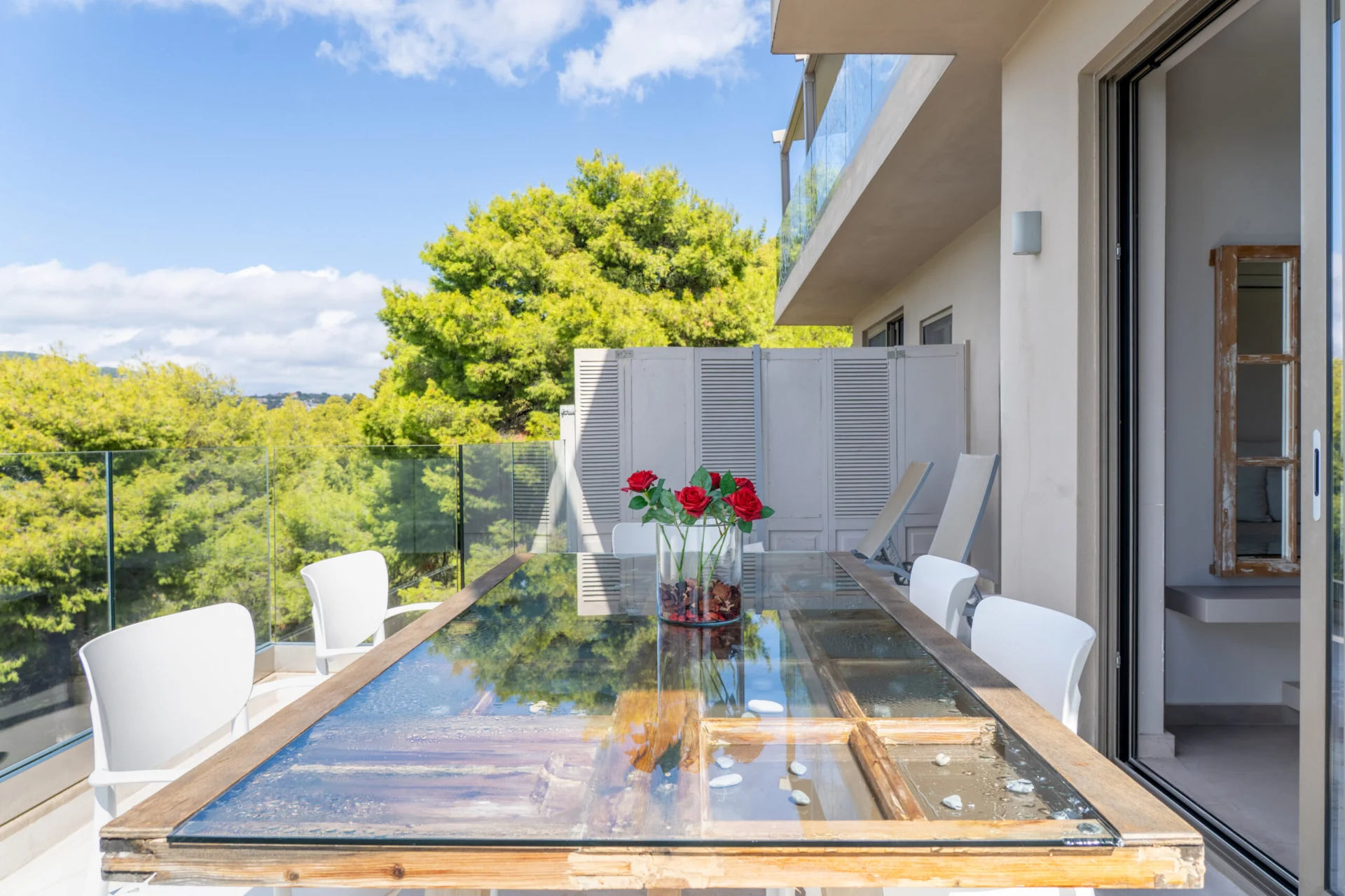 A glass dining table set with roses on the terrace, pines and the sea behind in the Daniel Signature Suite at CORE Luxury Suites, Skiathos.