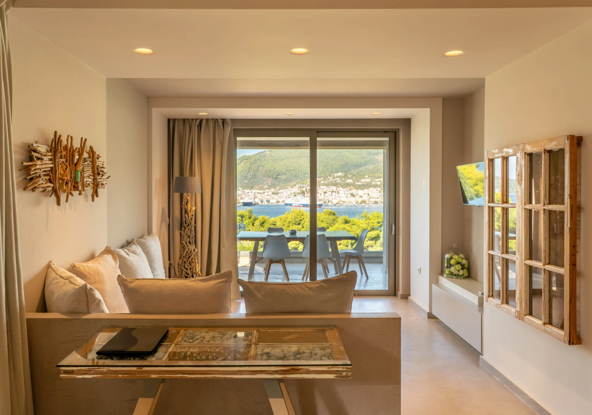 A living room with driftwood wall art and the bay through the glass doors in the Kassandra Signature Suite at CORE Luxury Suites, Skiathos.