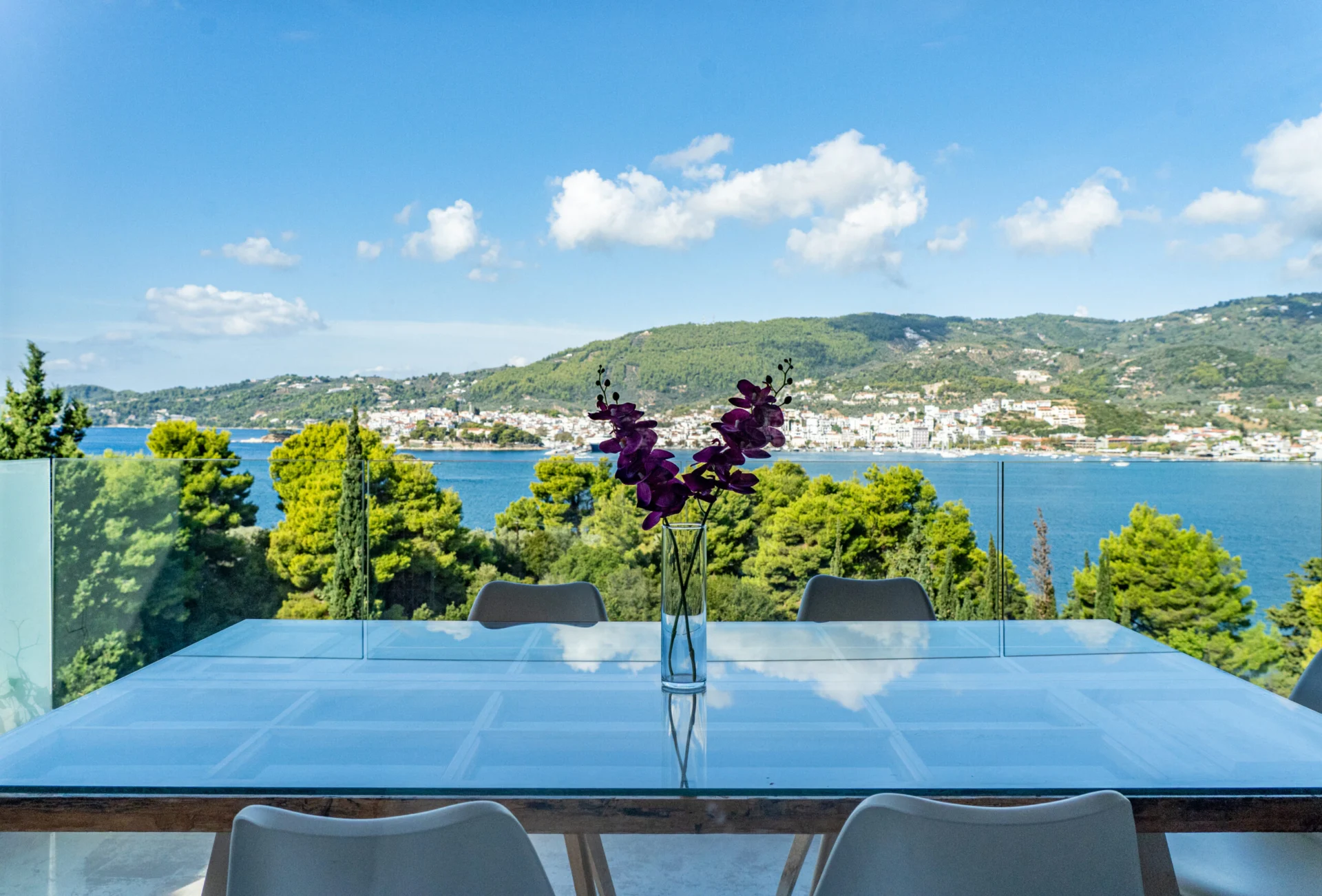 A glass terrace table with an orchid, the bay stretching out behind it in the Kassandra Signature Suite at CORE Luxury Suites, Skiathos.