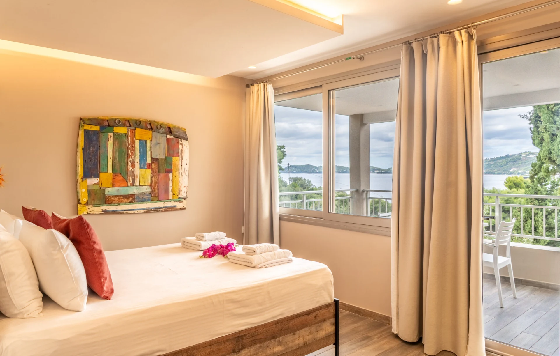 A bedroom with colourful artwork and the balcony door open to the sea in the Madalena Superior Suite at CORE Luxury Suites, Skiathos.