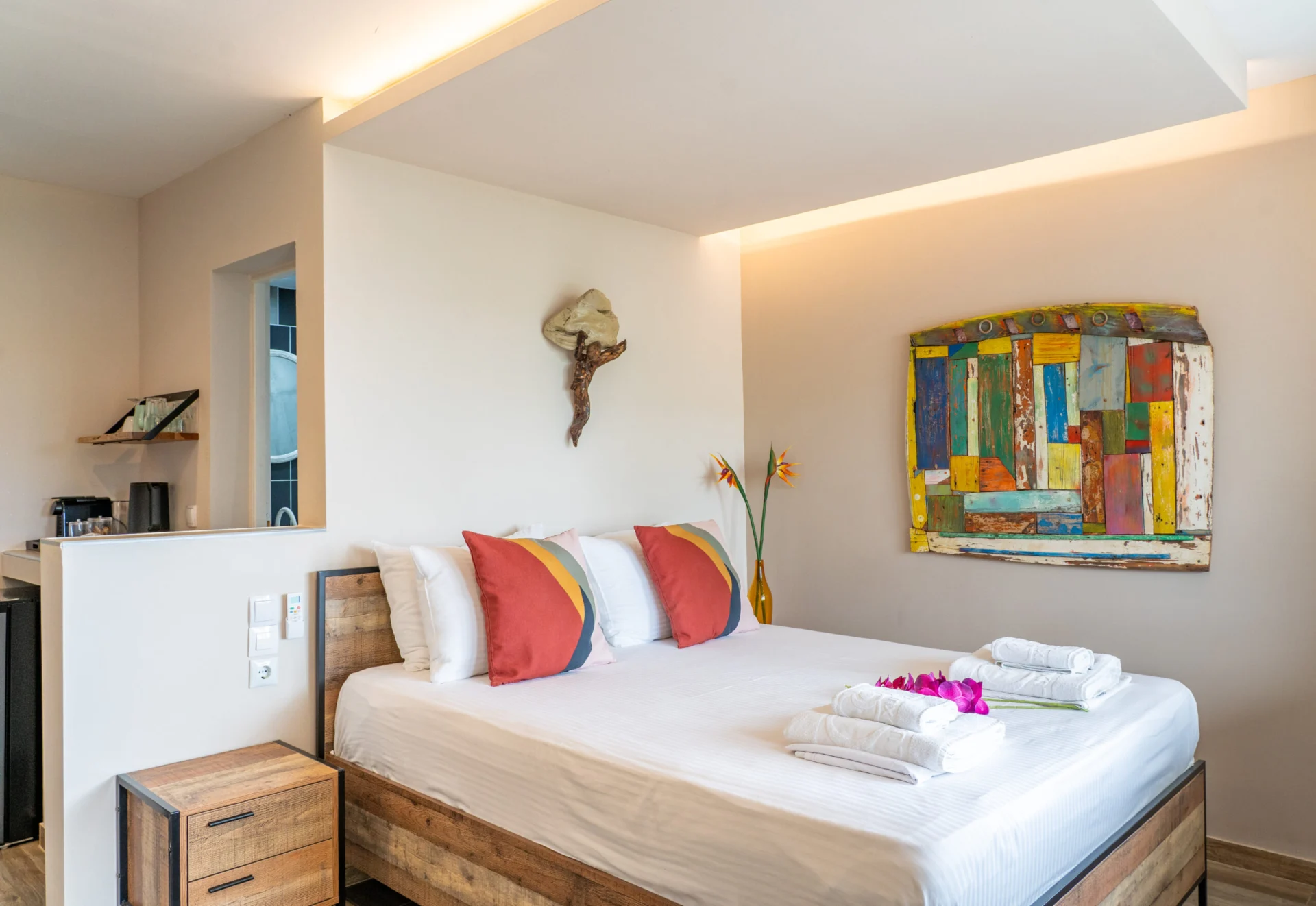 A bedroom with a driftwood sconce, painted artwork and the kitchenette in the Madalena Superior Suite at CORE Luxury Suites, Skiathos.