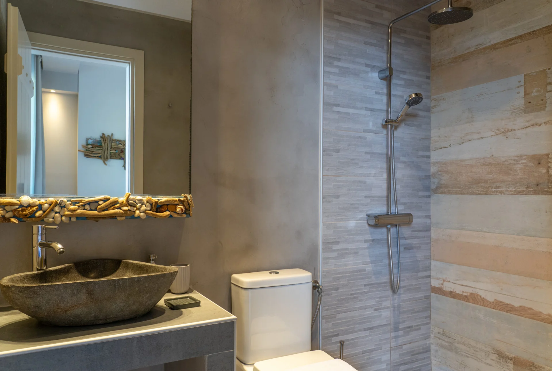 Un lavabo in pietra sotto uno specchio incorniciato in legno portato dal mare nella Vassiliki Deluxe Suite di CORE Luxury Suites, Skiathos.