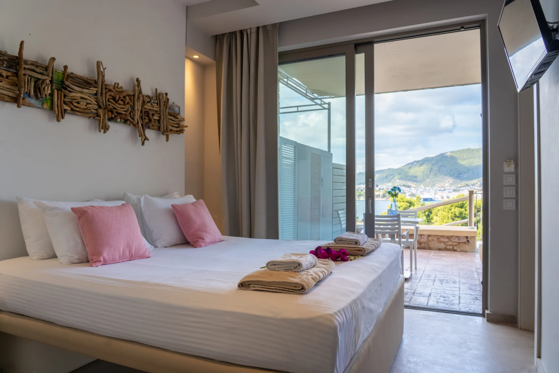 Ein Schlafzimmer mit Treibholzkunst und geöffneter Tür zur terrace mit Blick aufs Meer in der Vassiliki Deluxe Suite bei CORE Luxury Suites, Skiathos.