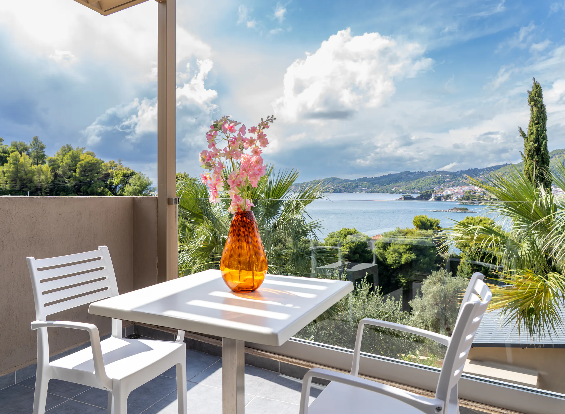Un tavolo sul balcony con un vaso color ambra e la baia sullo sfondo nella Alex 1 Classic Suite di CORE Luxury Suites, Skiathos.