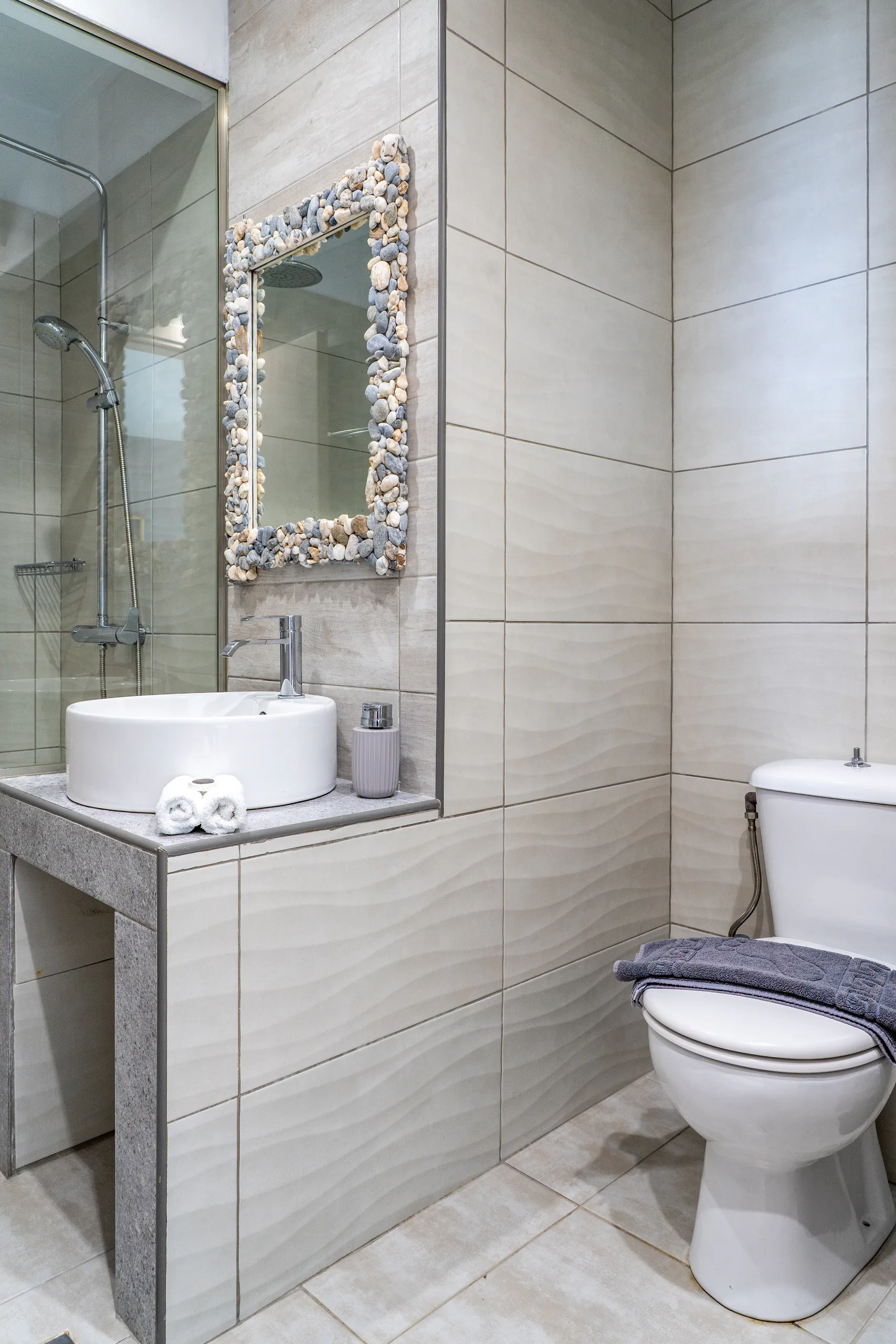 Un lavabo rotondo sotto uno specchio incorniciato da ciottoli e conchiglie nella Alex 1 Classic Suite di CORE Luxury Suites, Skiathos.