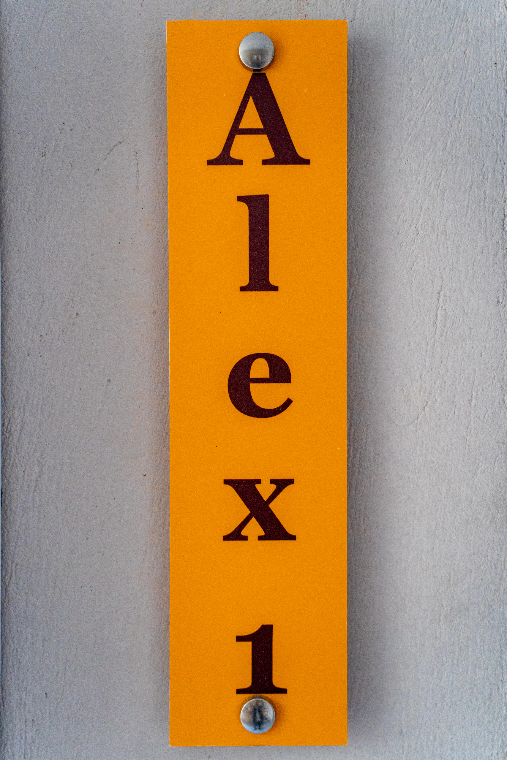 La targhetta verticale color ambra con il nome della suite, accanto alla porta della Alex 1 Classic Suite di CORE Luxury Suites, Skiathos.