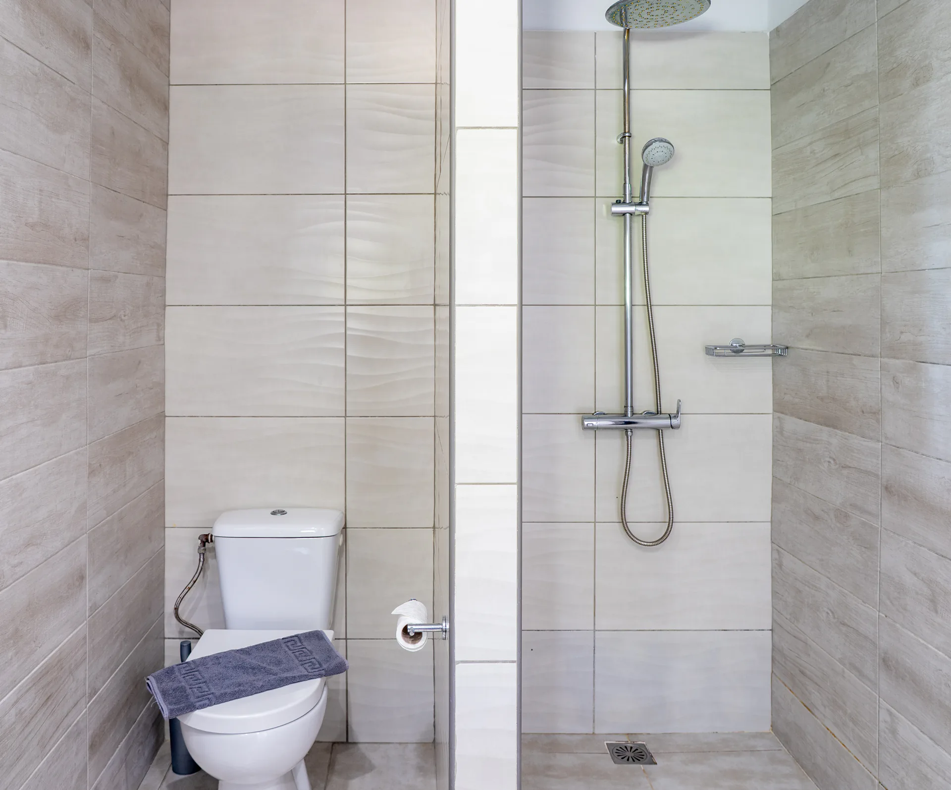 Una doccia walk-in dietro una parete di vetro, davanti a piastrelle dalla texture ondulata, nella Alex 2 Deluxe Suite di CORE Luxury Suites, Skiathos.