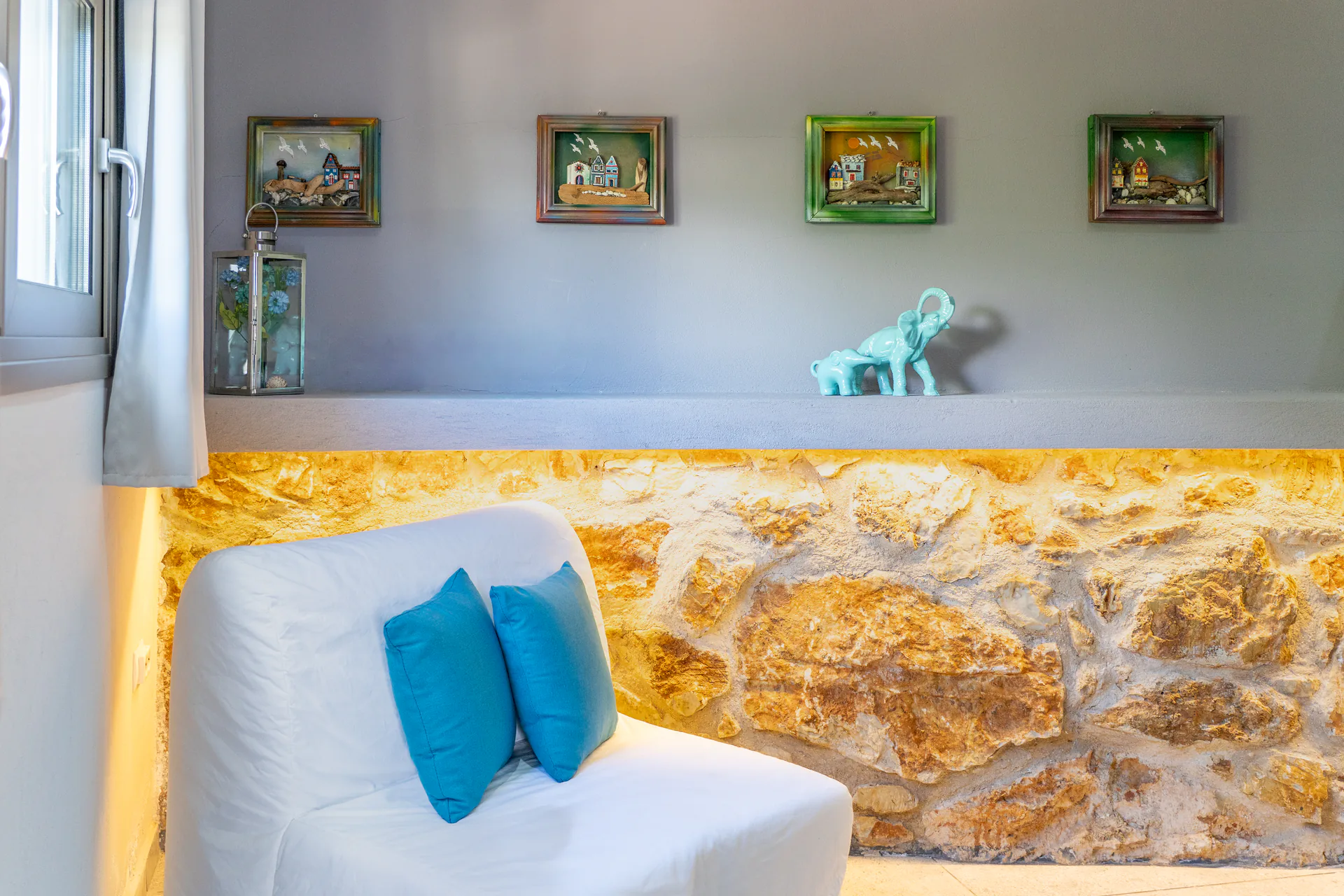Una poltrona con cuscini color ottanio davanti a una parete in pietra illuminata nella Alex 2 Deluxe Suite di CORE Luxury Suites, Skiathos.
