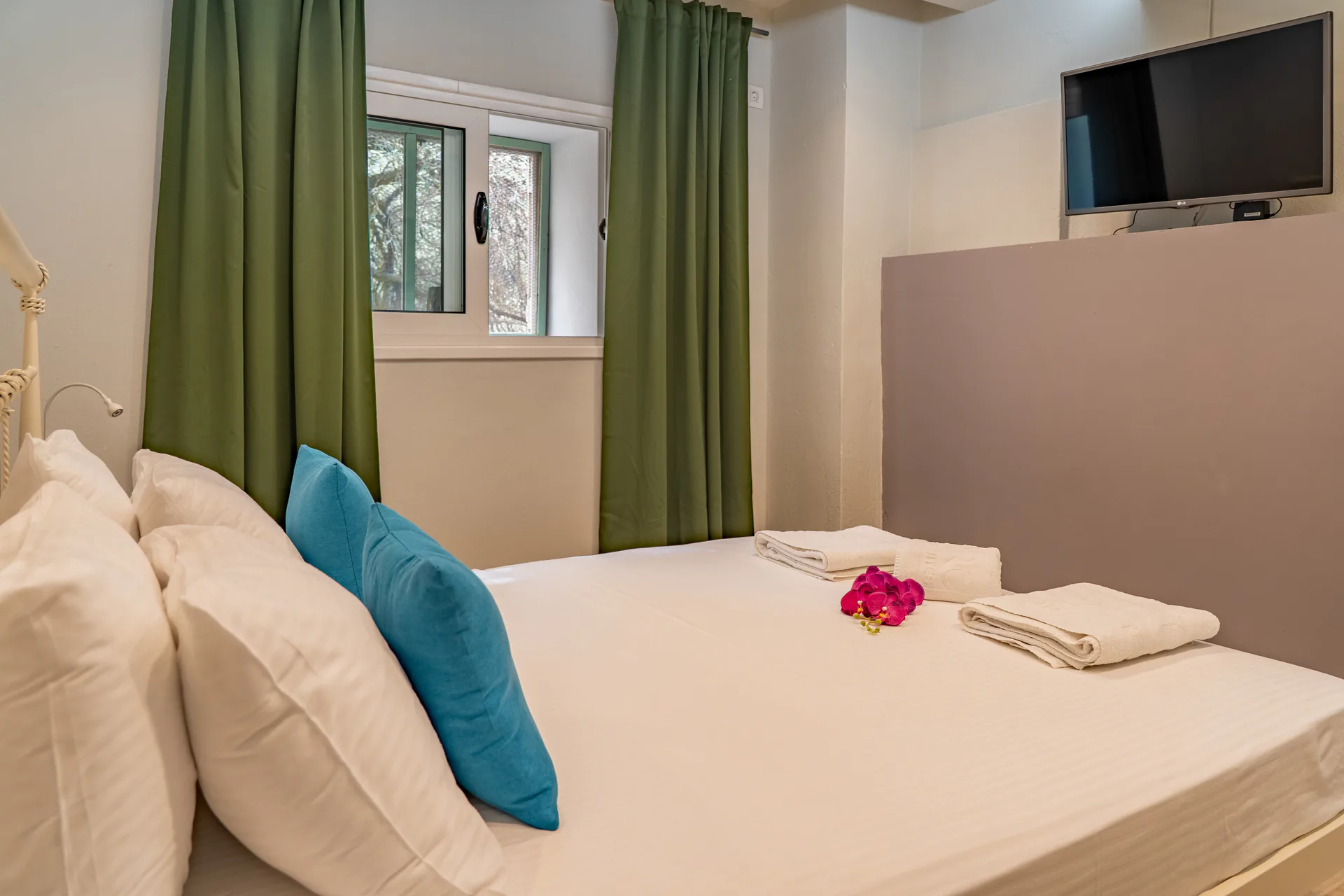 Un letto con cuscino cilindrico color ottanio sotto tende verdi nella Alex 3 Superior Suite di CORE Luxury Suites, Skiathos.
