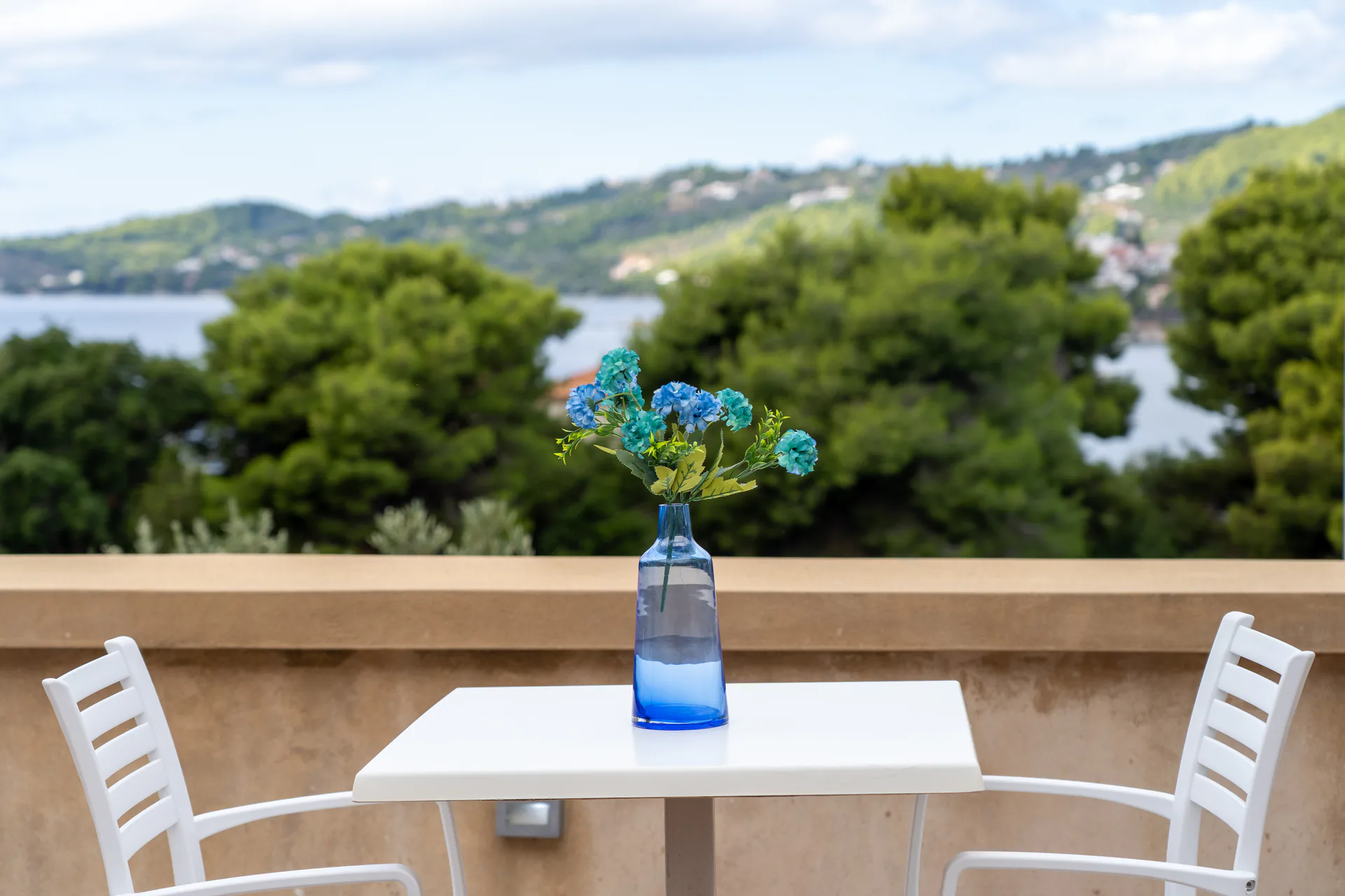 Un tavolo sulla terrace con un vaso in vetro blu e la baia sullo sfondo nella Alex 3 Superior Suite di CORE Luxury Suites, Skiathos.