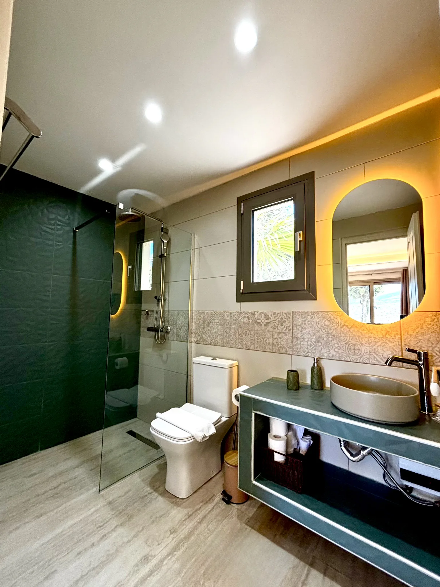 Eine ebenerdige Dusche mit tiefgrünen Fliesen unter einem hinterleuchteten Spiegel in der Cassy Deluxe Suite bei CORE Luxury Suites, Skiathos.