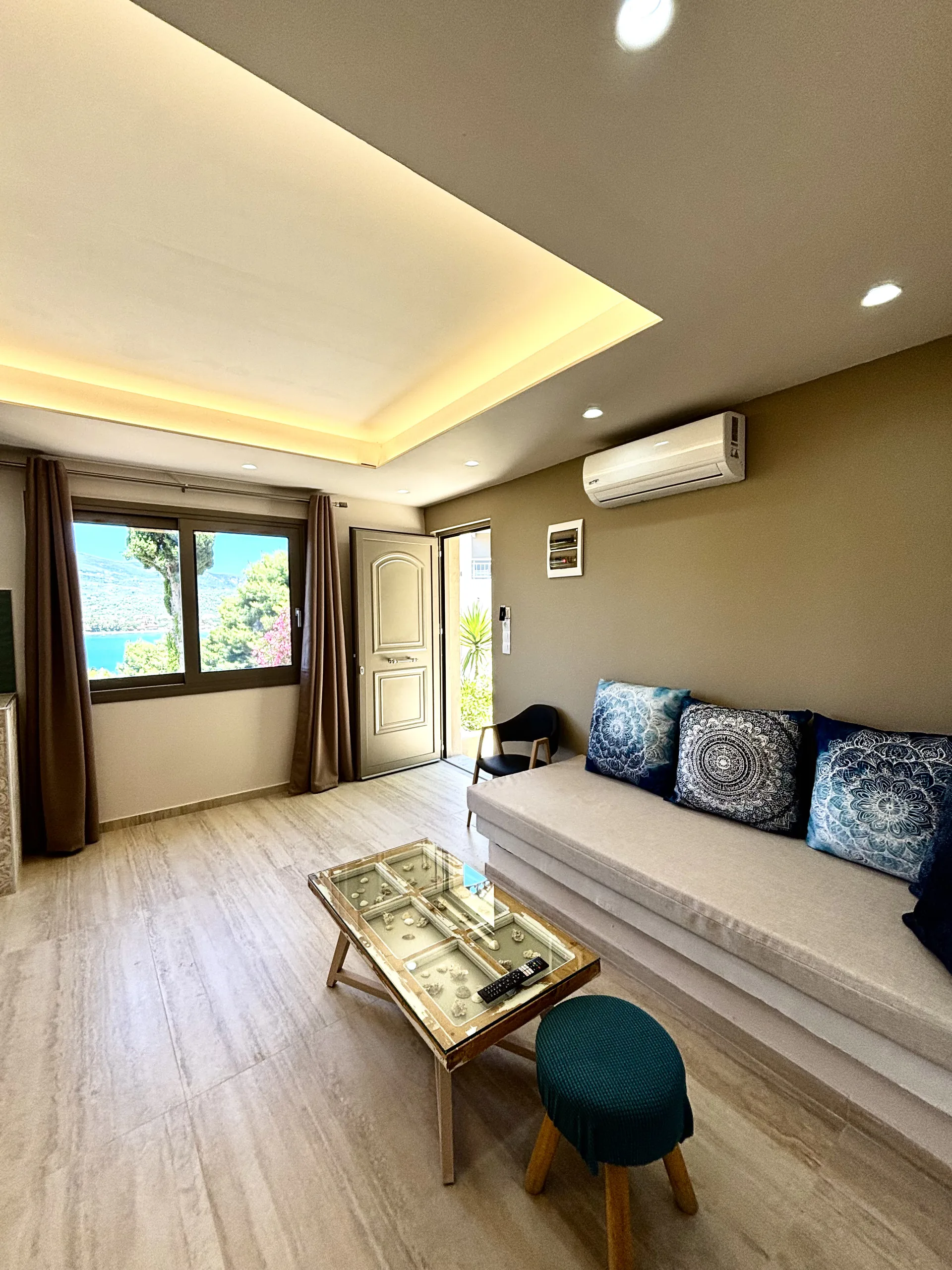 Ein Sofa mit blauen Kissen und zur Gartenanlage geöffneter Eingangstür in der Cassy Deluxe Suite bei CORE Luxury Suites, Skiathos.