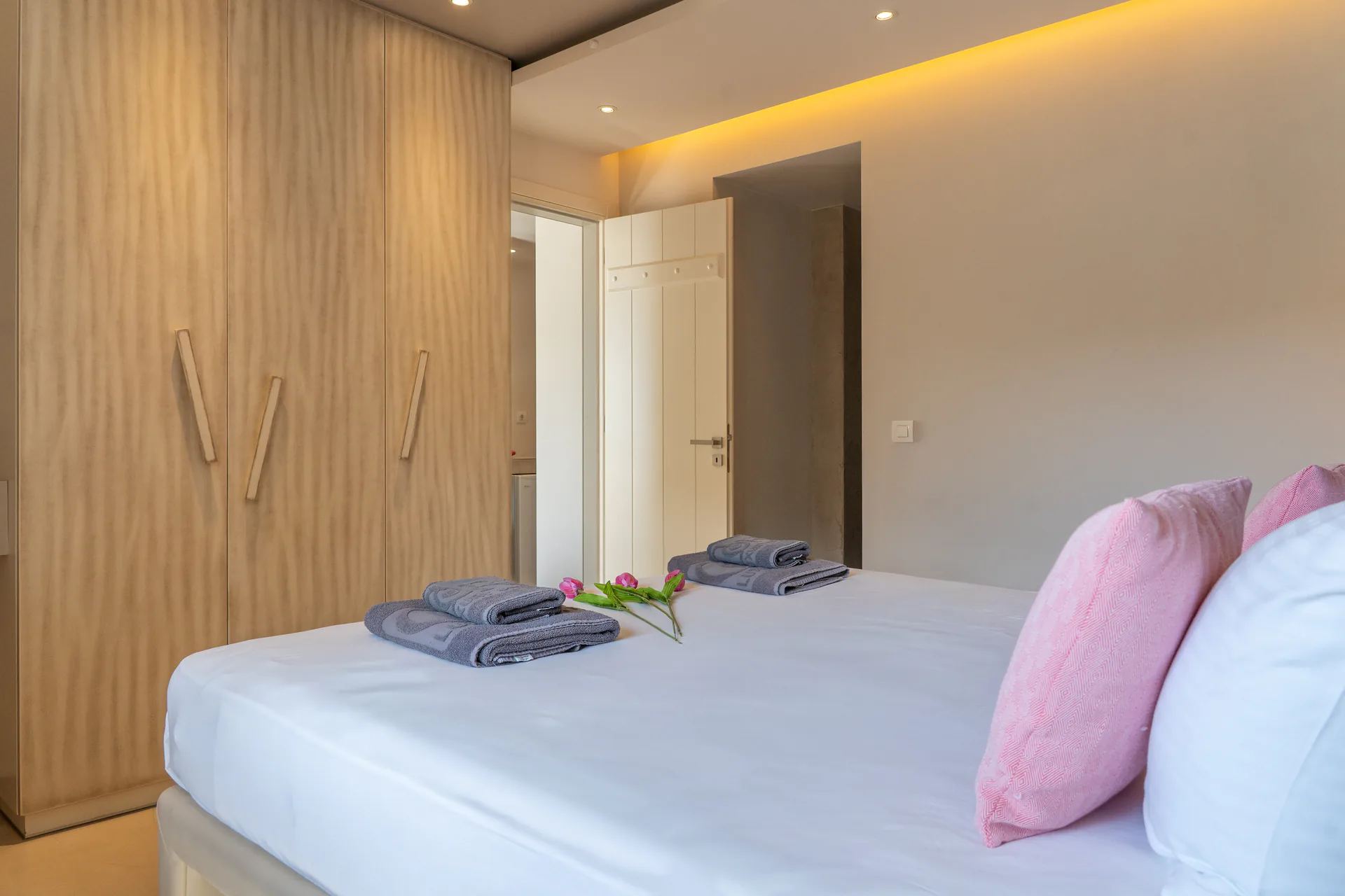 Ein Bett mit rosafarbenen Kissen gegenüber einer Wand aus hellen Eichenschränken in der Daniel Signature Suite bei CORE Luxury Suites, Skiathos.
