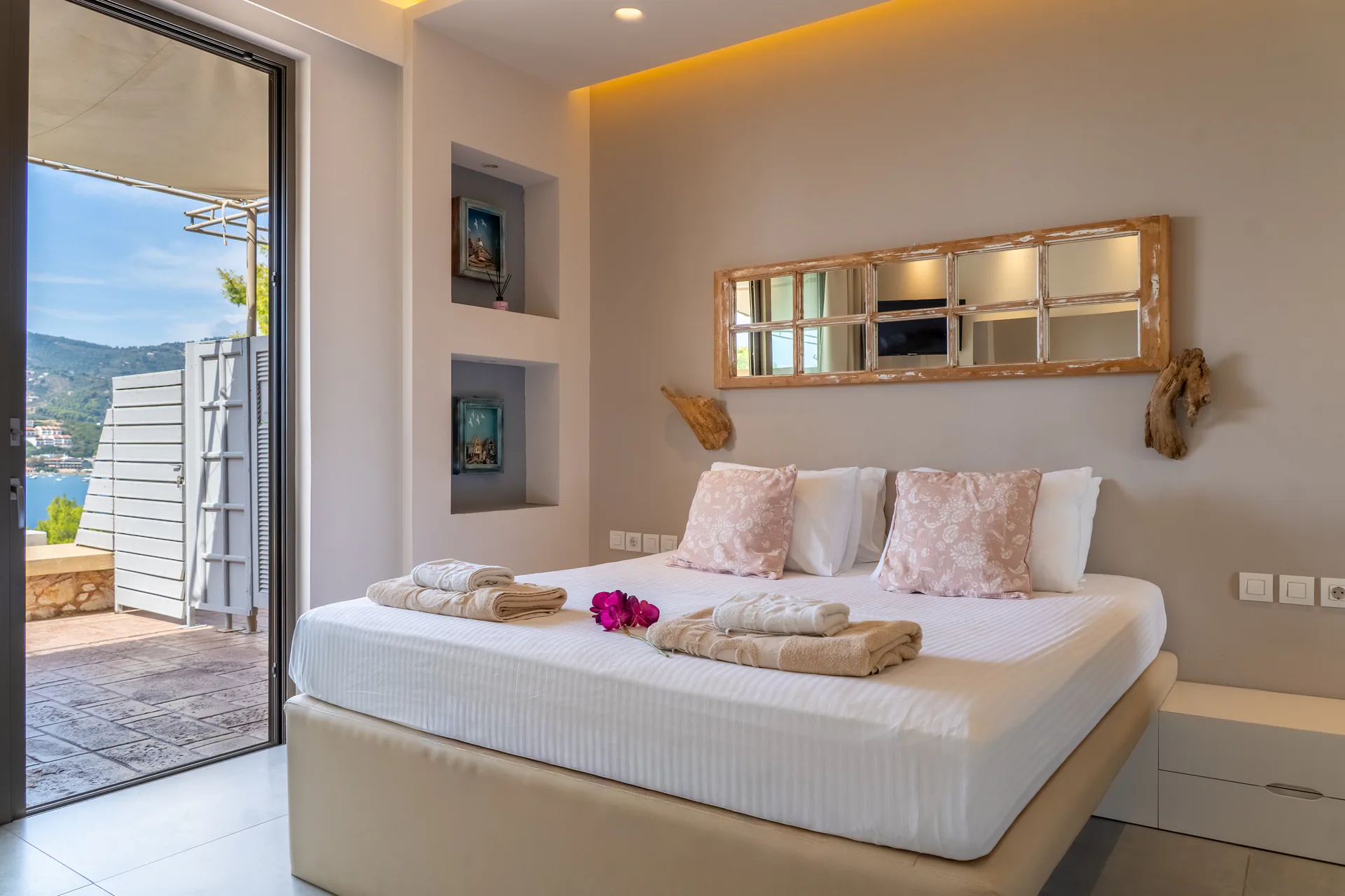 A bed below a mirrored panel, the terrace door open to the bay in the Demi Classic Suite at CORE Luxury Suites, Skiathos.