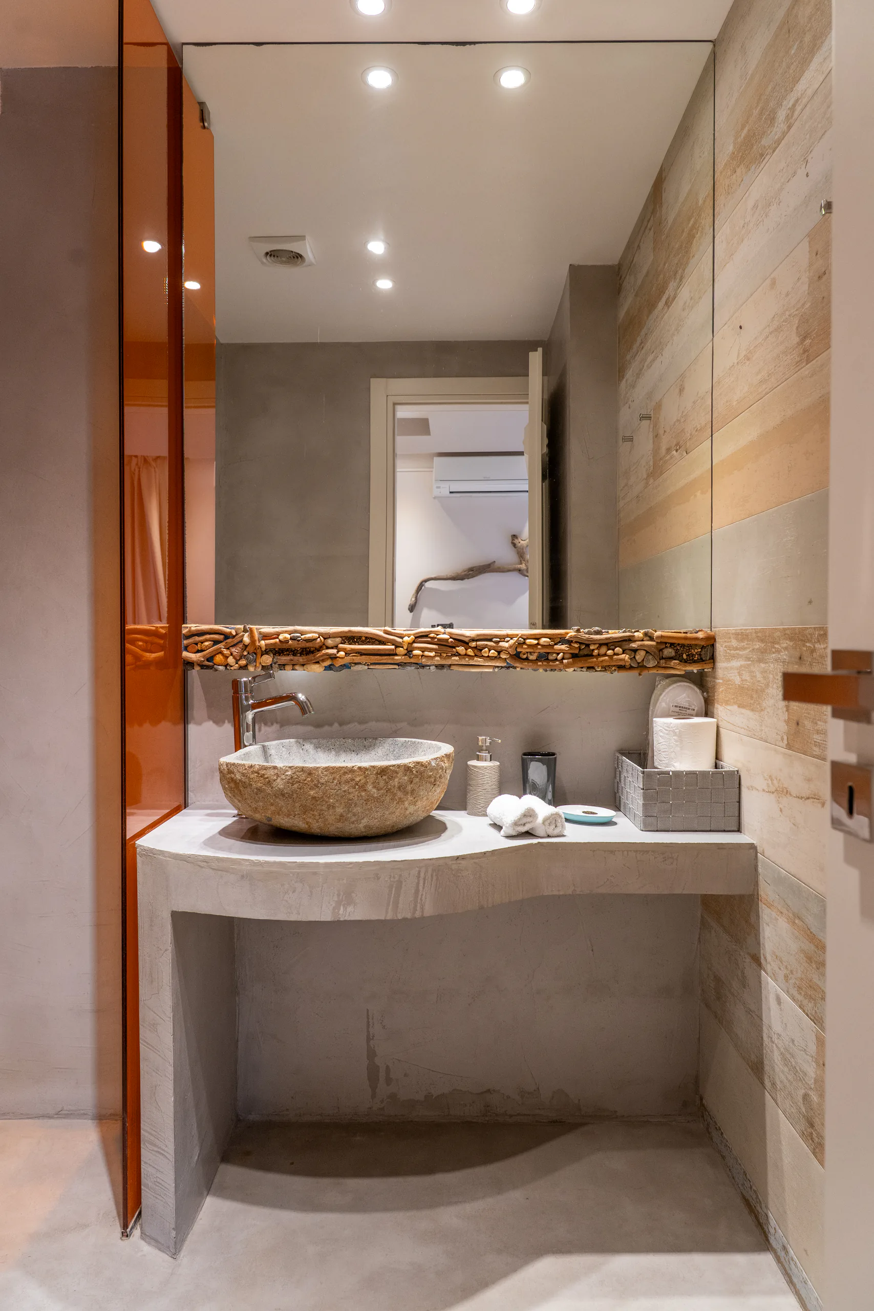 A stone basin on a curved concrete vanity below driftwood in the Kassandra Signature Suite at CORE Luxury Suites, Skiathos.