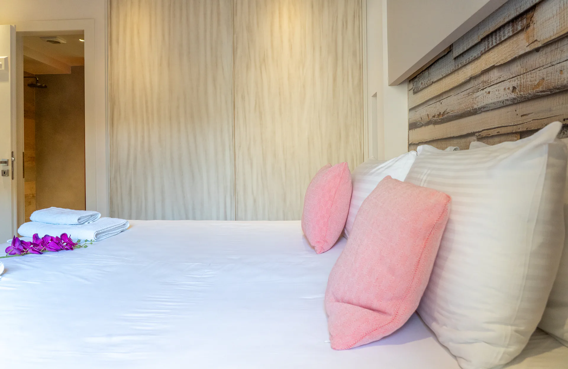 A bed with coral cushions and a driftwood headboard in the Kassandra Signature Suite at CORE Luxury Suites, Skiathos.