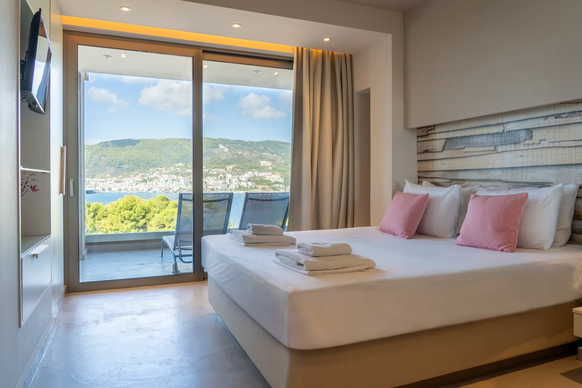 A bed facing sliding doors open to the bay in the Kassandra Signature Suite at CORE Luxury Suites, Skiathos.