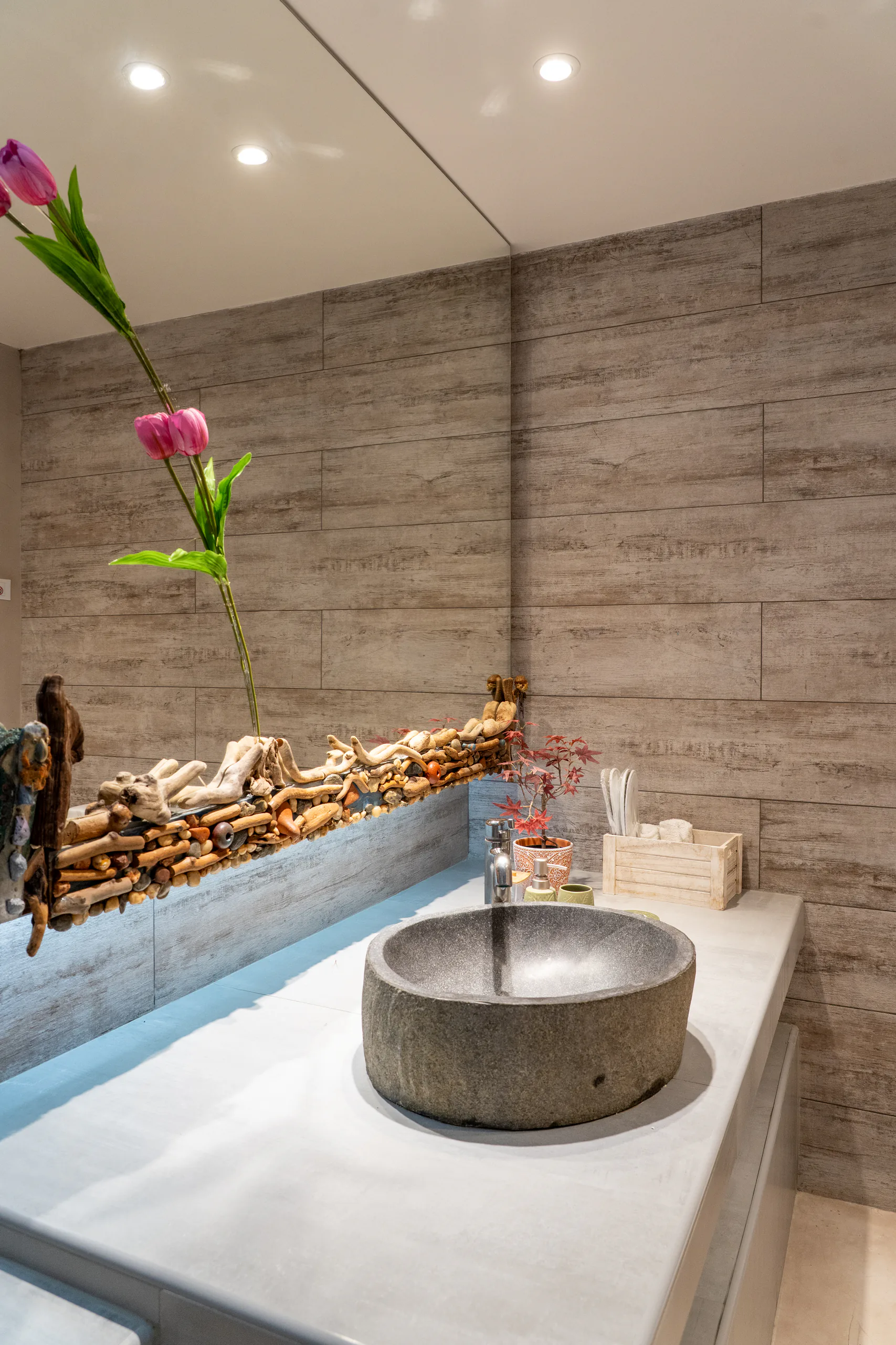 A stone bowl basin below a driftwood shelf, tulips beside it in the Maggi Superior Suite at CORE Luxury Suites, Skiathos.