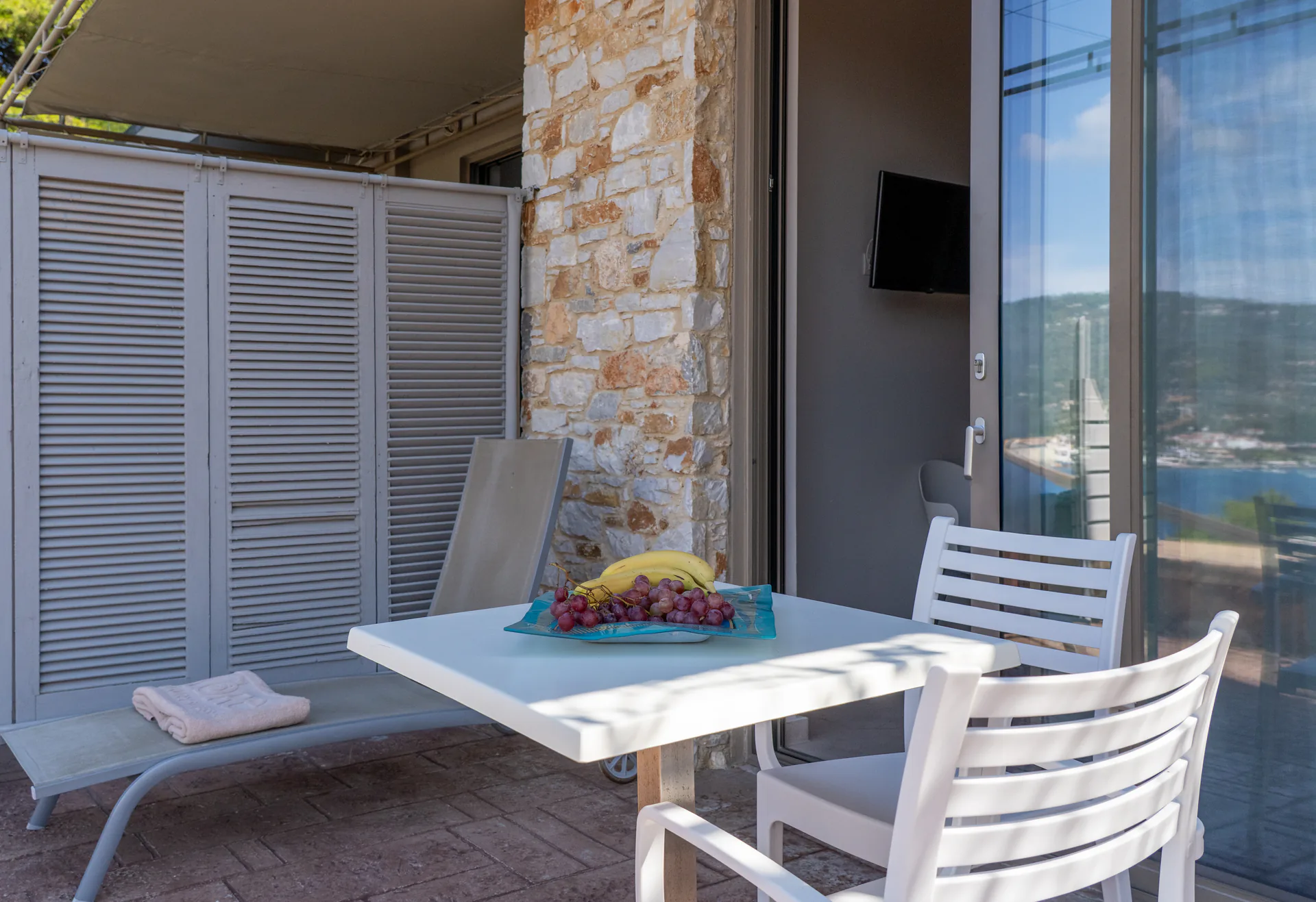A terrace table and lounger under the awning by a stone pillar in the Maggi Superior Suite at CORE Luxury Suites, Skiathos.