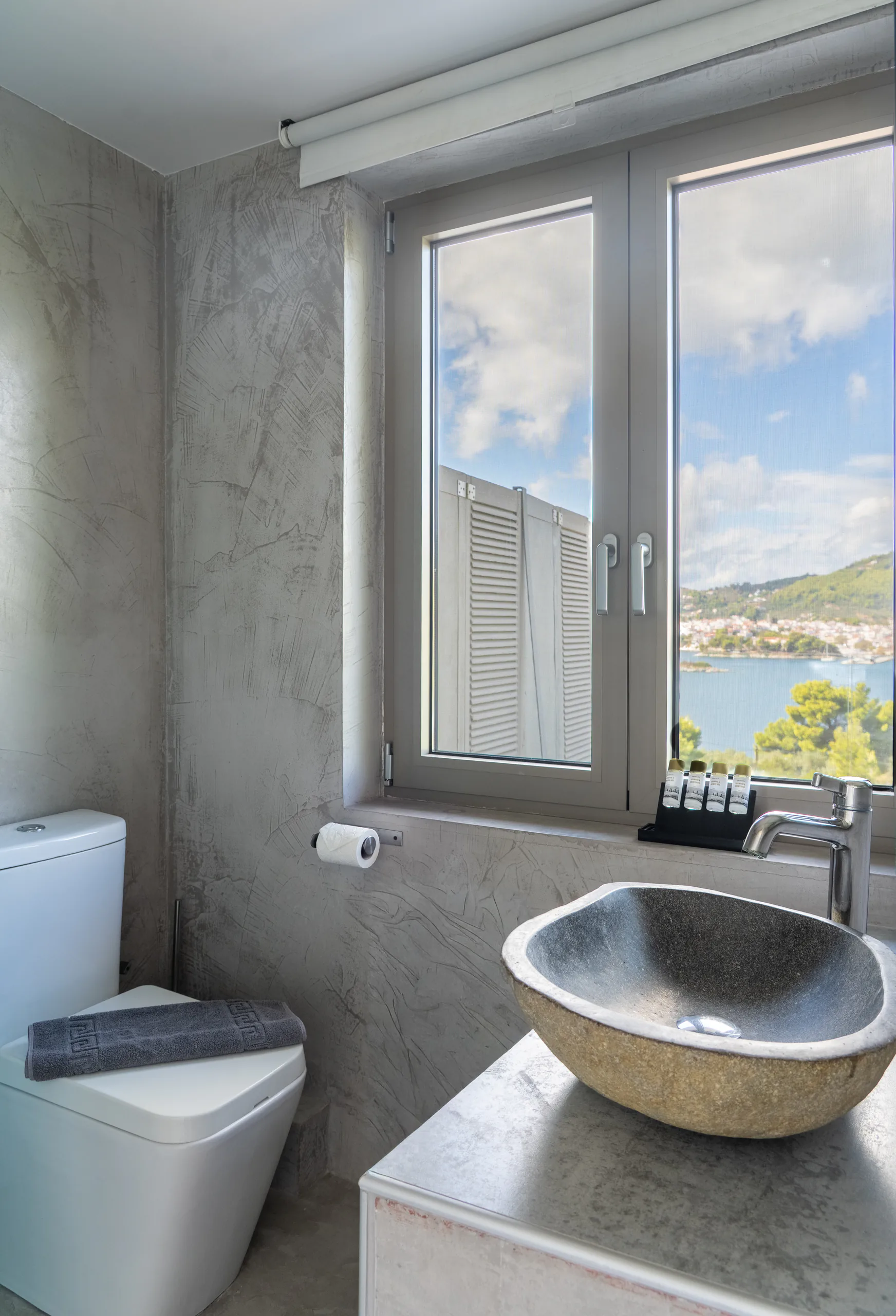 A stone bowl basin below a window onto the bay in the Patrick Family Suite at CORE Luxury Suites, Skiathos.
