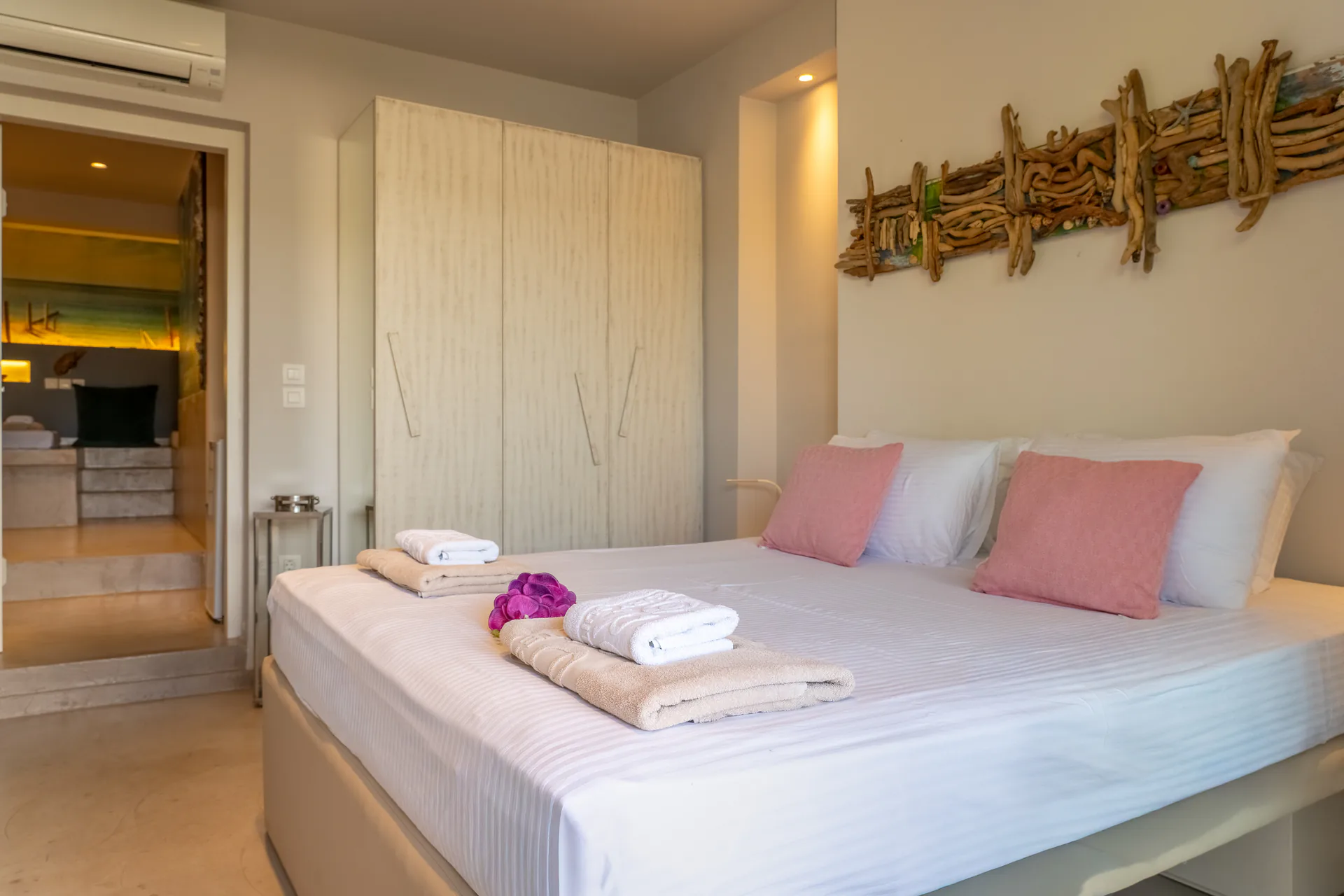 Un letto con cuscini rosa sotto un pannello in legno portato dal mare nella Vassiliki Deluxe Suite di CORE Luxury Suites, Skiathos.